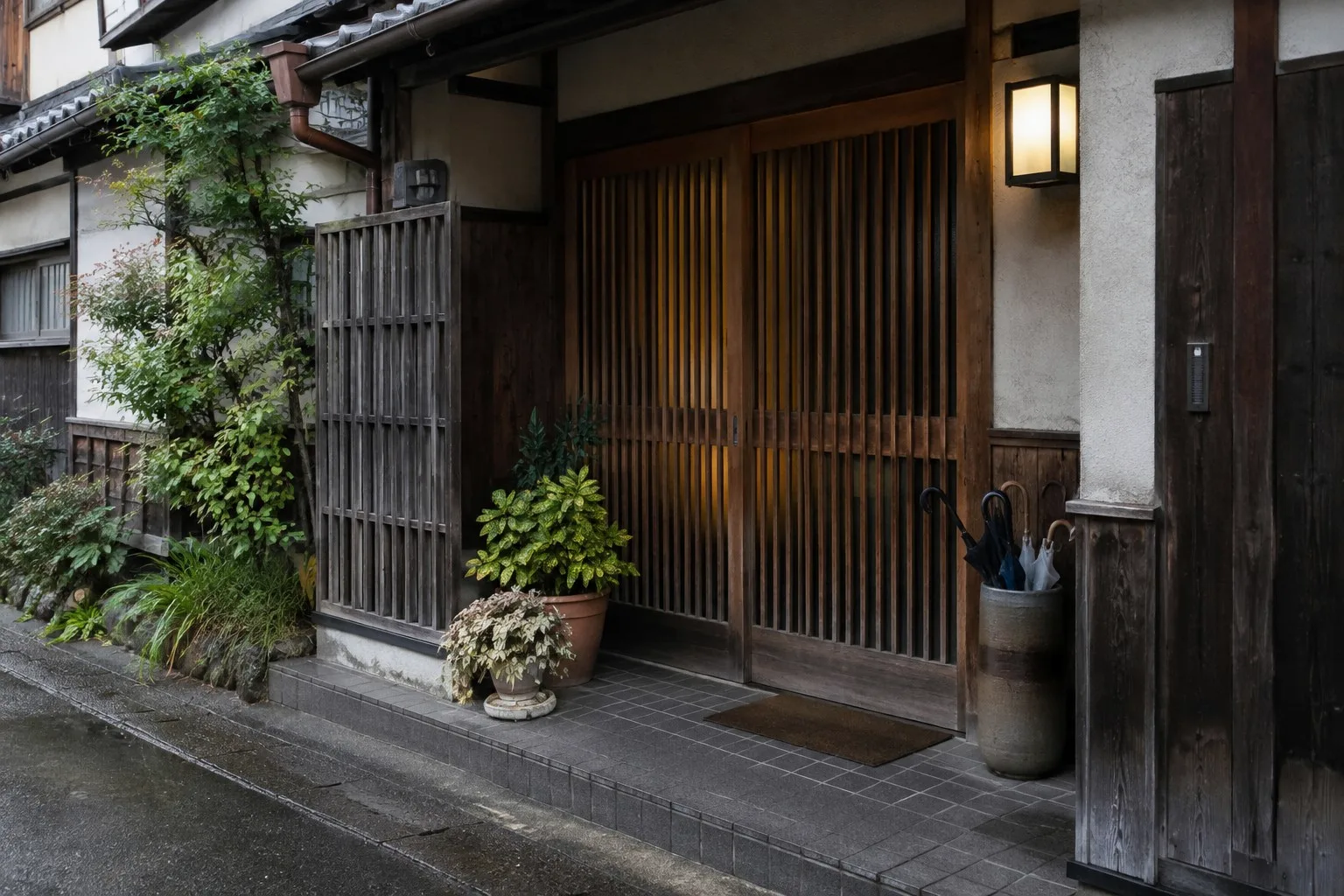 The entrance of a small Japanese guesthouse with wooden doors and an umbrella stand