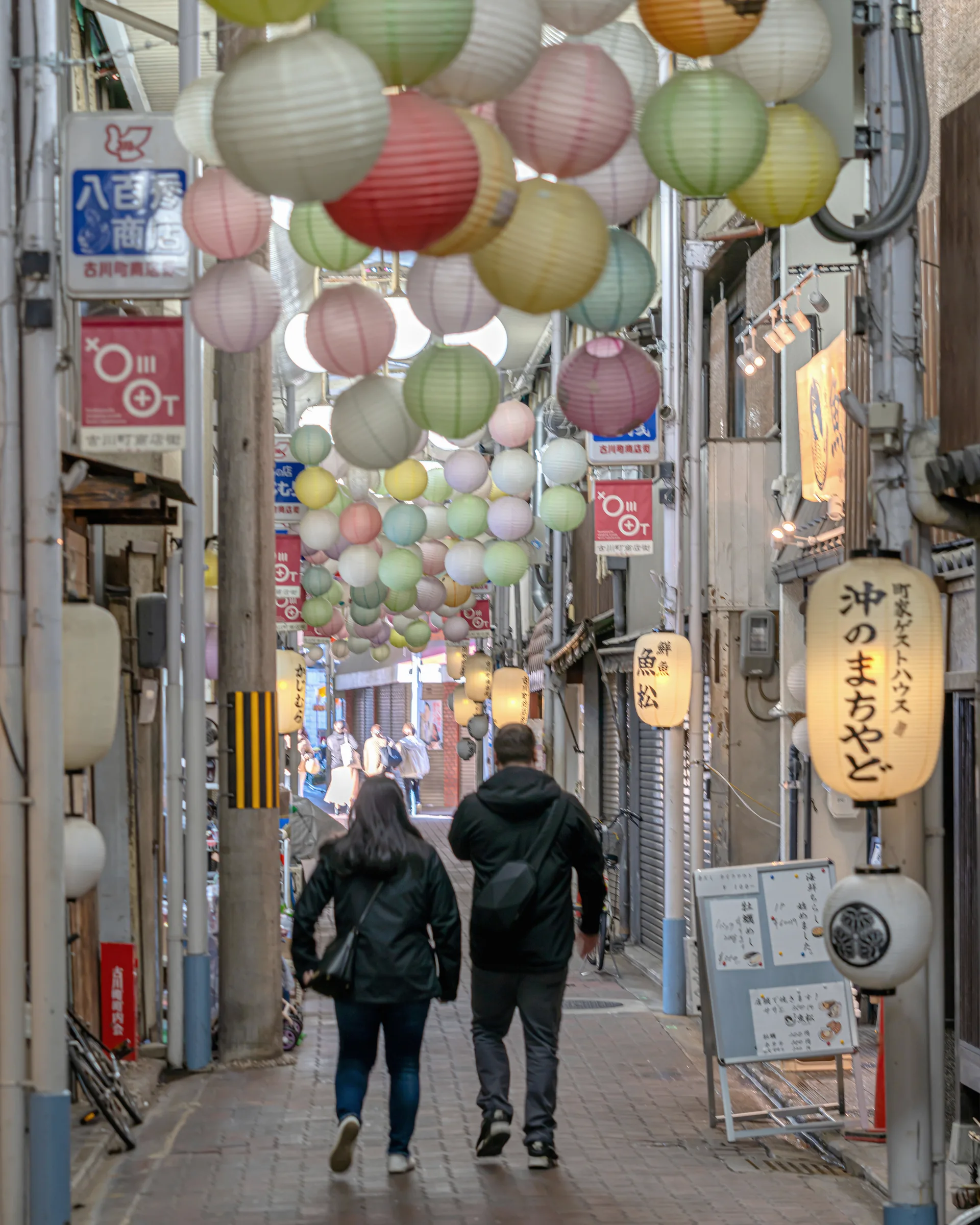 Two travelers walking beneath paper lanterns in a neighborhood alley