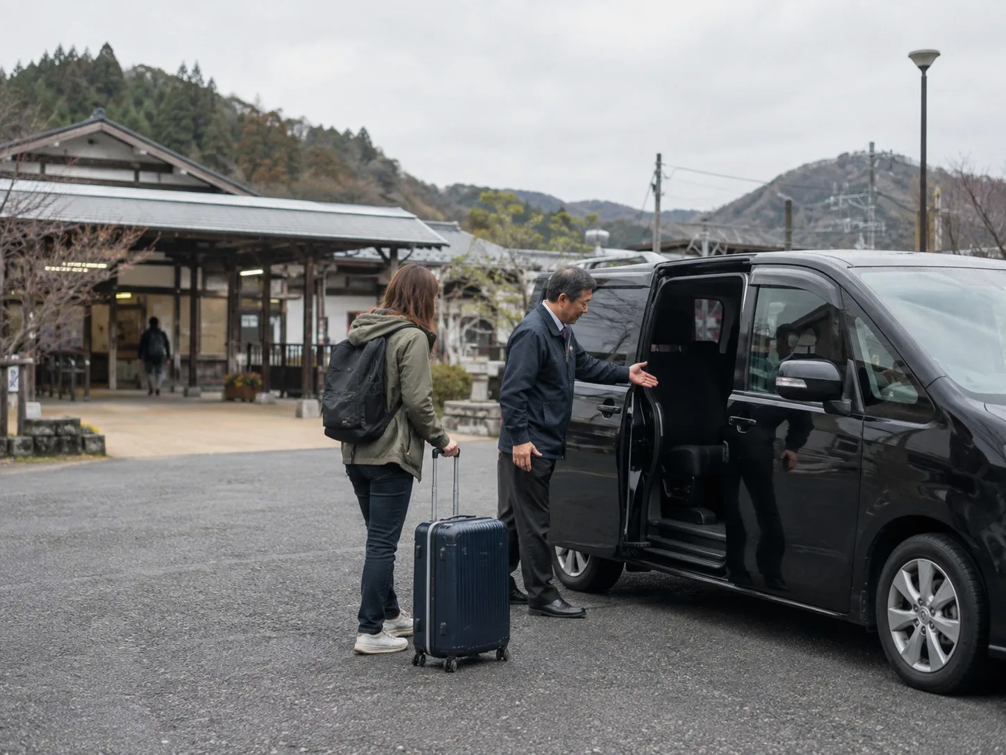 A traveler with luggage being welcomed beside a private vehicle at a small station